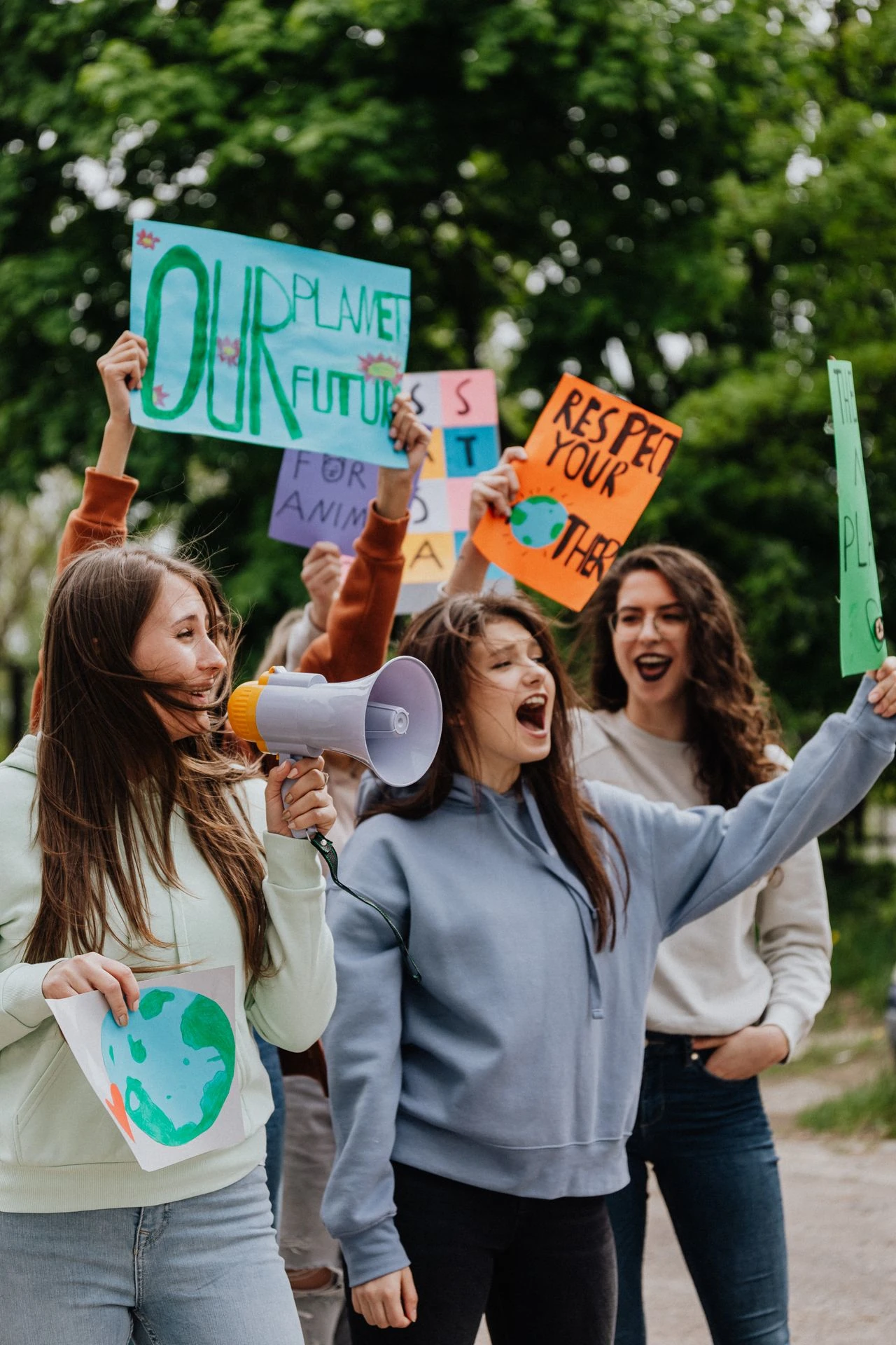 Group of young women holding signs and megaphone advocating for environmental action outdoors
